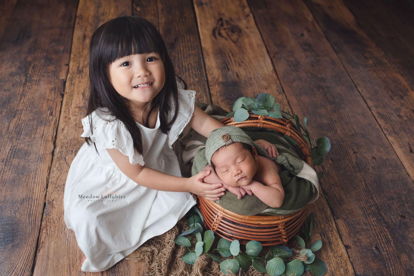 Sister posing with her newborn brother sleeping in rattan crate prop