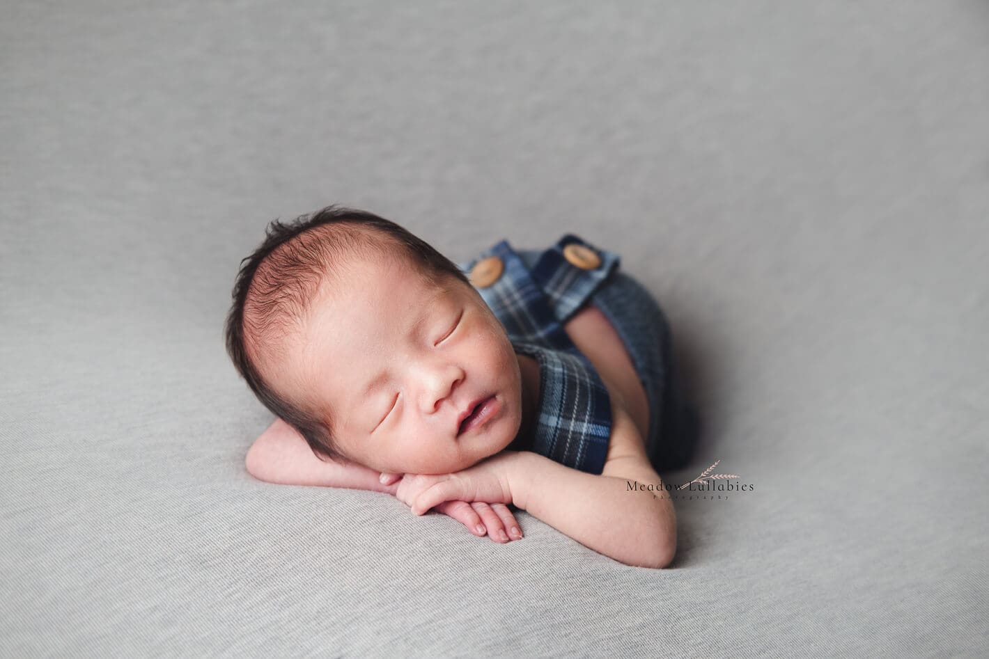 Newborn photography - Baby in cute blue outfit posing on plain surface