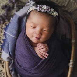 Newborn photography singapore Newborn photography smiling baby wrapped in purple sleeping in a rattan basket prop