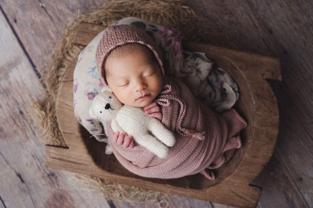 Baby girl holding soft toy bear in crate prop