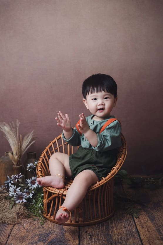 Baby photoshoot: 10 months old baby clapping hands sitting on vintage rattan chair