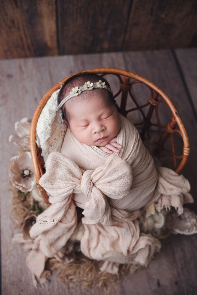 Newborn Photography Singapore | Meadow Lullabies Newborn baby in neutral tone beige bow ribbon wrap sleeping on rattan chair prop